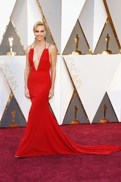 a woman in a red gown on the oscars red carpet with her dress pulled back