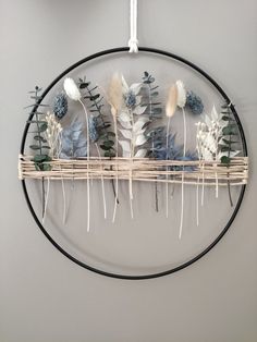 a circular wall hanging with dried flowers and leaves on the top, in front of a gray wall