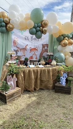 an outdoor dessert table set up with balloons and woodland animals on the wall behind it