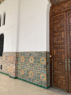 an ornately decorated wall and door in front of a white building with wooden doors