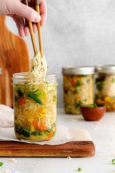 someone holding chopsticks over a mason jar filled with noodles and veggies