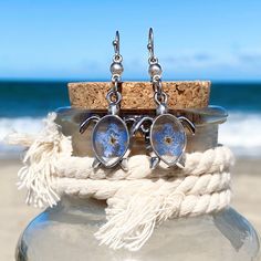 Transport yourself to the tranquil shores with our enchanting Forget Me Not Sea Turtle Earrings, blending playful charm with coastal elegance. Crafted with exquisite detail, they capture the essence of sun-kissed beaches and azure waves. Whether lounging by the shore or exploring coastal treasures, these earrings are a delightful keepsake for any beach enthusiast. Remind your loved ones of sunny days and seaside adventures with this perfect accessory, guaranteed to add a touch of oceanic magic t Elegant Adjustable Jewelry For Beach Season, Blue Ocean-inspired Jewelry For Vacation, Ocean-inspired Jewelry With Lobster Clasp For Vacation, Ocean-inspired Sterling Silver Beach Jewelry, Ocean-inspired Jewelry For Vacation With Lobster Clasp, Coastal Adjustable Jewelry For Beach Season, Adjustable Coastal Jewelry For Beach Season, Summer Sterling Silver Jewelry With Matching Earrings, Sterling Silver Jewelry With Matching Earrings For Summer