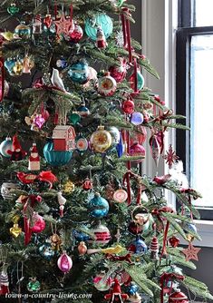 a christmas tree with ornaments hanging from it's branches in front of a window