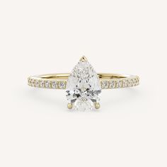 a yellow gold engagement ring with a pear shaped diamond in the center and pave set shoulders