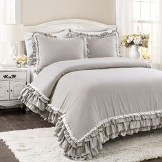 a white bed with ruffled bedspread and pillows in a bedroom next to a window