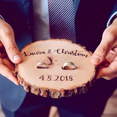 two hands holding a piece of wood with wedding rings on it and the ring holder is engraved