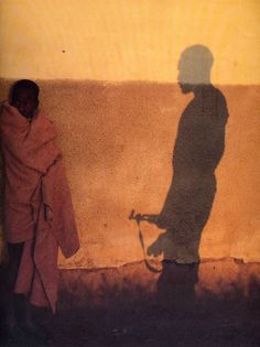 a man standing next to a wall with his shadow on the wall and a bike leaning against it