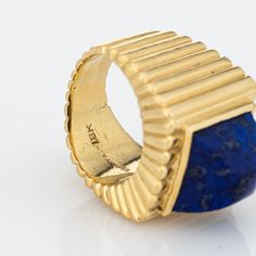 This is part of Chairish’s Fine Jewelry assortment.  Vintage Tiffany & Co lapis lazuli ring crafted in 18 karat yellow gold (circa 1970s).    Lapis lazuli measures 11mm diameter. The lapis is in good condition with some minor abrasions visible under a 10x loupe.  Dating to the 1970s the 18k gold ring is styled in a ridged square design. The sugarloaf cut cobalt blue lapis lazuli makes a great statement. The ring is a great example of 70s era design with a bold, distinct look that makes an impact Luxury Formal Jewelry With Fluted Bezel, Luxury Yellow Gold Cabochon Signet Ring, Luxury Yellow Gold Signet Ring With Cabochon, Modernist Yellow Gold Rings For Formal Occasions, Hallmarked Modernist Yellow Gold Jewelry, Modernist Hallmarked Yellow Gold Jewelry, Luxury Rings With Fluted Bezel For Gift, Luxury Yellow Gold Sapphire Ring Stamped 14k, Luxury 14k Yellow Gold Sapphire Ring