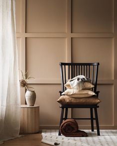 a chair sitting in front of a window next to a rug and vase with flowers