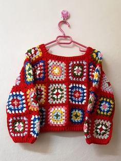 a red crocheted sweater hanging on a white wall next to a pink hanger