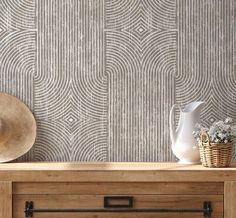 a white vase sitting on top of a wooden table next to a wallpapered wall