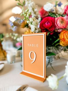 the table number is displayed on an orange and white card holder with flowers in it