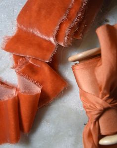 an orange piece of cloth is next to a pair of wooden clothes pins on a white surface