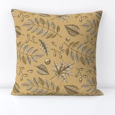 a decorative pillow with leaves and berries on the front is shown in gold, black and white