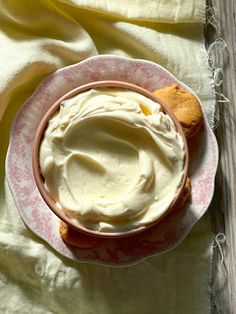 a pink and white plate topped with cream next to cookies on top of a table