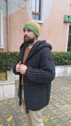 a man with a beard wearing a knitted hat and jacket standing in front of a building