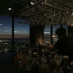 a man standing at a bar with lots of glasses in front of him and looking out the window