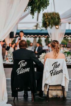 a man and woman sitting at a table with their back to the camera, both wearing black jackets