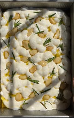 a pan filled with food covered in white sauce and topped with pine nuts on top