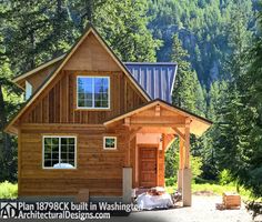 a small wooden cabin in the woods with mountains in the backgrouds and trees around it