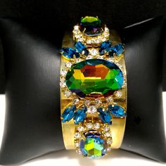 *Description: This is a gorgeous watermelon rhinestone crystal bracelet on a golden brass cuff which glitters and sparkles in the light. The vintage rhinestones are secured on a golden brass cuff and the reflective cuff adds additional sparkle to the bracelet. There is one large watermelon rhinestone in the center, surrounded by clear rhinestones and sapphire blue marquise cut rhinestones. On each side of the center stone are two more watermelon rhinestones, a little smaller in size, one on each Jeweled Party Bracelet, Party Jeweled Bracelet Jewelry, Luxury Jeweled Bracelet For Parties, Crystal Bracelet With Jewels For Parties, Crystal Bracelets With Jewels For Parties, Party Crystal Bracelets With Jewels, Glamorous Jeweled Bracelets For Party, Green Stone Bracelets For Party, Crystal Bangle Cuff Bracelet For Party