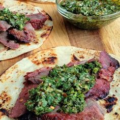 some tacos with meat and green sauce on top of them next to a bowl of pesto