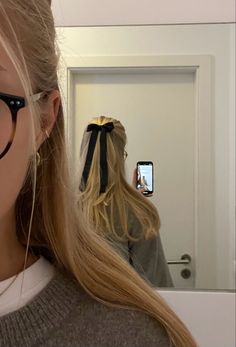 a woman wearing glasses taking a selfie in front of a mirror with her cell phone