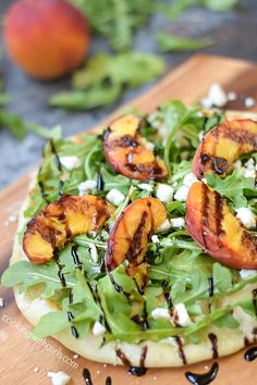 a pizza topped with grilled peaches and spinach on top of a wooden cutting board