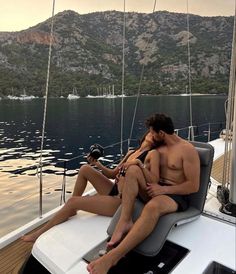 a man and woman sitting on the back of a sailboat taking a selfie