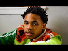 a young man with dreadlocks sitting in front of a wall and looking at the camera