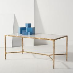 a glass table with gold frame and blue blocks on the top, in front of a white wall