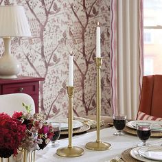 a dining room table is set with place settings and candlesticks, along with red flowers