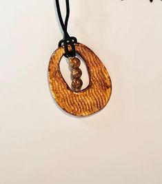 a wooden pendant with two beads hanging from it's side on a black cord