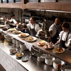 chefs preparing food in a restaurant kitchen with stainless steel counter tops and white brick walls