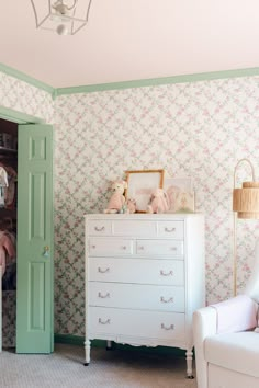 a baby's room with pink and green wallpaper, a white dresser and teddy bears