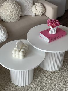 two white tables with flowers on them in front of a couch