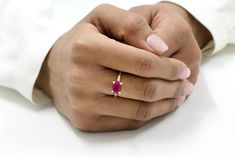 a close up of a person's hand holding a ring with a ruby stone