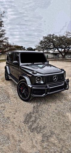 a black mercedes g - class is parked in the gravel