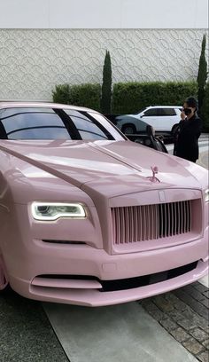 a pink rolls royce parked in front of a building with people looking at the car