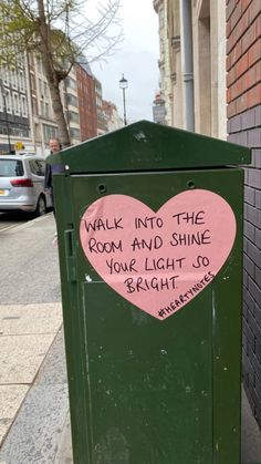 a green trash can with a pink heart painted on it's side next to a brick wall