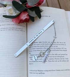 an open book with a silver bar and two charms on it next to a bouquet of flowers