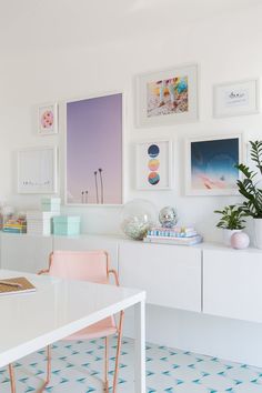 a white dining room table with pink chairs and pictures on the wall above it,