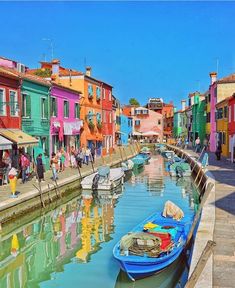 boats are docked in the water next to colorful buildings and people walking on the sidewalk