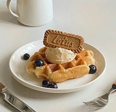 a waffle topped with ice cream and blueberries on a plate next to a fork