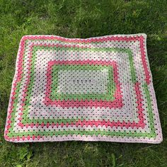 a crocheted blanket laying on the grass in front of some green and pink flowers