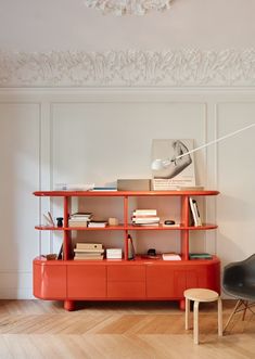 an orange shelf with books on it in a white room next to a black chair