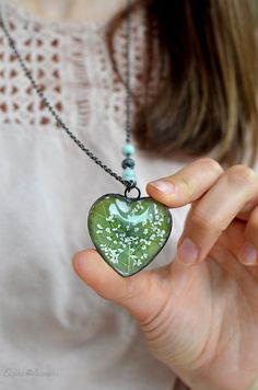 a woman holding a green heart shaped pendant with white flowers on it's side