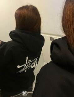 two women in black hoodies are looking at their cell phones while sitting on the toilet