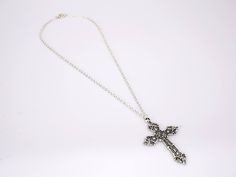 The cross pendant of this lovely piece is an elegantly crafted piece with many charming accents adorning it. It's forged from a strong 316L stainless steel material and finished in a polished silver coat. The exterior border and detailed outlines on this piece are smooth and clean-cut, while the interior India is covered in a rougher, granite-like surface. The contrasting textures are clear and highlight the details on the piece beautifully. The cross stands at 56 mm long. This Innovato Design piece comes with a 18" silver twisted Singapore chain.  Product Highlights:    Made from durable stainless steel silver  Elegant Cross Pendant Design  Twisted Singapore Chain Necklace (Length: 18") Metal Crucifix Cross Necklace As Gift, Metal Crucifix Cross Necklace Gift, Metal Crucifix Cross Necklace For Gift, Gothic Silver Pendant Cross Necklace, Spiritual Metal Cross Necklace, Nickel-free Metal Cross Pendant Jewelry, Metal Cross Pendant Necklace, Spiritual Metal Cross Pendant Necklace, Spiritual Metal Pendant Cross Necklace