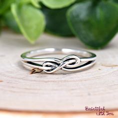 a silver ring sitting on top of a piece of wood next to green leaves and greenery